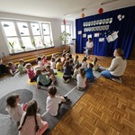 Dzieci siedzą na sali gimnastycznej i słuchają czytanej bajki 