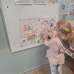 Dziewczynka dokleja elementy do pracy plastycznej na tablicy 