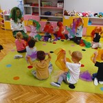 dzieci siedzą na dywanie z panią która na kolorową chustkę na głowie.jpg