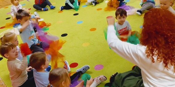dzieci siedzą na dywanie i machaja kolorowymi chustkami.jpg