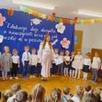 dzieci stoją w eleganckich ubraniach razem z panią w różowej spódnicy.jpeg