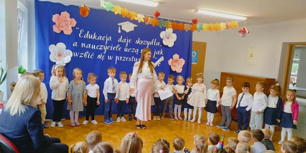 dzieci stoją w eleganckich ubraniach razem z panią w różowej spódnicy.jpeg