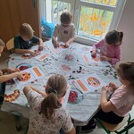 dzieci siedzą przy stoliku i wyklejają szablon dyni.jpg