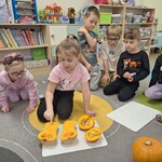 dzieci siedzą na dywanie dziewczynka pokazuje palcem na przekrojoną dynię.jpg
