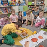 dzieci siedzą na dywanie a chłopiec kłądzie dynię na wagę.jpg