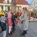 nauczycielka zapala znicz obok stoją dzieci.jpg