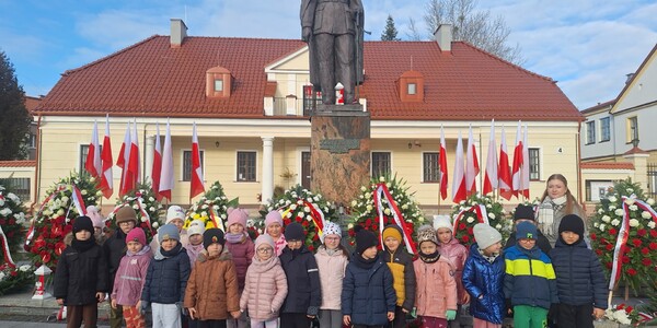 dzieci razem z nauczycielką stoją pod pomnikiem.jpg