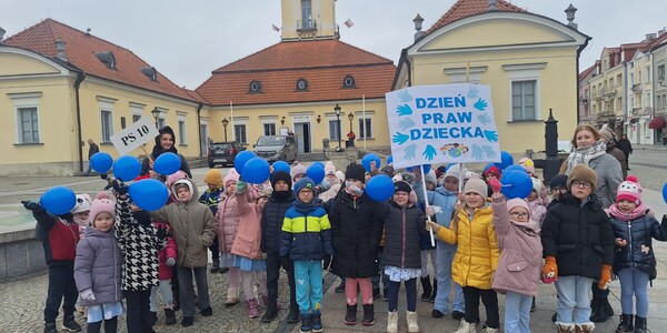 dzieci i panie stoją przed ratuszem z niebieskimi balonami.jpg