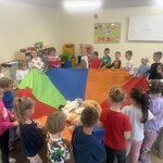dzieci trzymają kolorową chustę na której leżą pluszowe misie.jpg