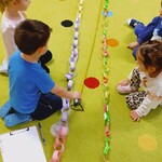 dzieci siedzą na dywanie i mierzą papierowy łańcuch.jpg