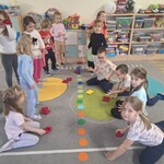 dzieci stoją i siedzą na dywanie przed nimi leżą kolorowe kółka.jpg