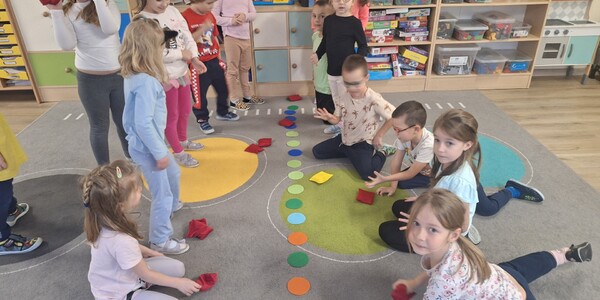 dzieci stoją i siedzą na dywanie przed nimi leżą kolorowe kółka.jpg