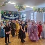 Dzieci ubrane w stroje karnawałowe stoją na tle napisu Bal Karnawałowy i dekoracji z balonów 