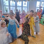 Dzieci przebrane w stroje karnawałowe tańczą podnosząc ręce do góry.