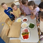dzieci stoją przy stole na którym leżą produkty do zrobienia pizzy.jpg