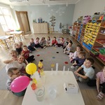 Dzieci siedzą w kole i obserwują doświadczenia 
