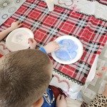 Chłopiec maluje niebieską farbą po talerzu z mlekiem