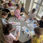 Dzieci siedząc przy stolikach projektują ubrania.