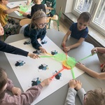 Dzieci używając packi klepią w kartkę z naklejonymi muchami.