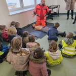 dzieci siedzą na podłodze ratownik klęczy przy manekinie.jpg