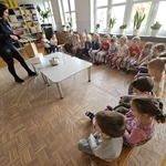 dzieci siedzą na ławeczkach przed nimi stoi pani w granatowej bluzie.jpg