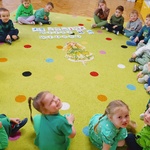 dzieci siedzą na dywanie przy obrazku dziewczynki w zielonej sukience.jpg