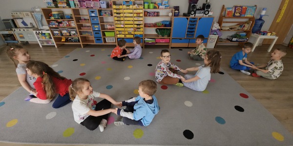 dzieci siedzą na dywanie w parach na przeciwko siebie i trzymają się za ręce.jpg