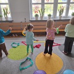 dzieci stoją na dywanie na którym leżą kolorowe szarfy.jpg