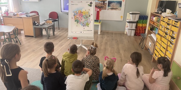 dzieci siedzą na dywanie i oglądają kolorową mapę Polski.jpeg