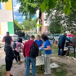panie nakładają z garnka bigos mężczyzna przewraca kiełbaski na grillu.jpeg