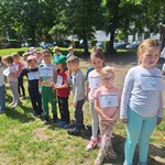 dzieci stoją na trawie z przyczepionymi kartkami.jpg