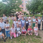 dzieci stoją lub siedzą na trawie z białymi kartkami.jpg