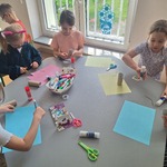 dzieci siedzą przy stoliku wycinają kolorowe kartki papieru.jpg