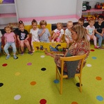 dzieci siedzą na dywanie nauczycielka siedzi na krześle i czyta dzieciom książkę.jpg