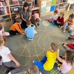 dzieci siedzą na dywanie i patrzą na kolorową planszę z emocjami.jpeg
